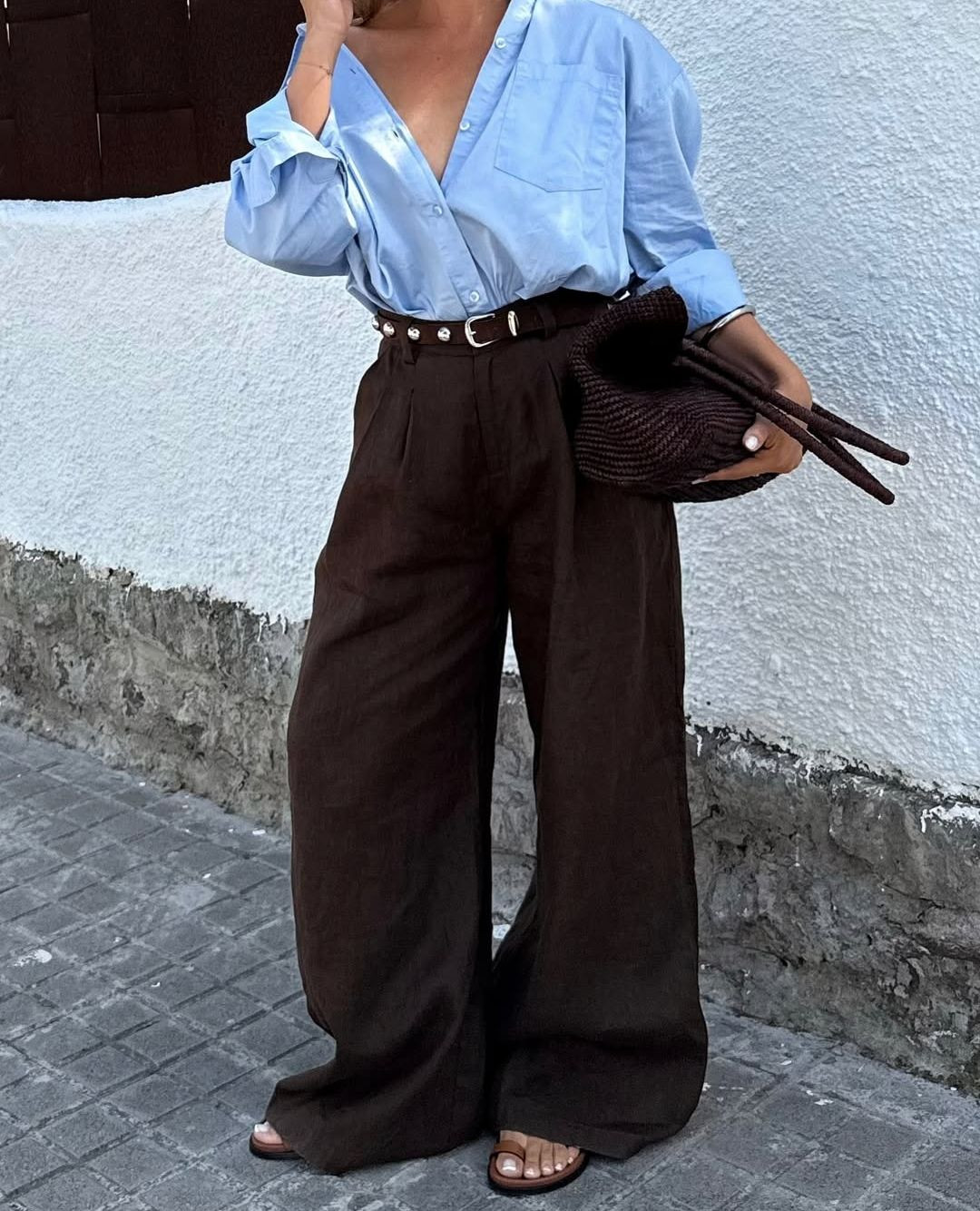 Foto de uma mulher usando um look composto por camisa azul, cal&ccedil;a marrom e bolsa marrom