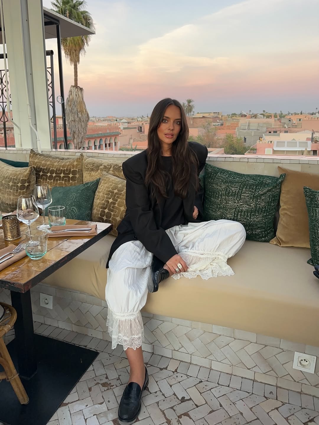 Foto de uma mulher morena usando um look composto por blazer preto, cal&ccedil;a branca e mocassim