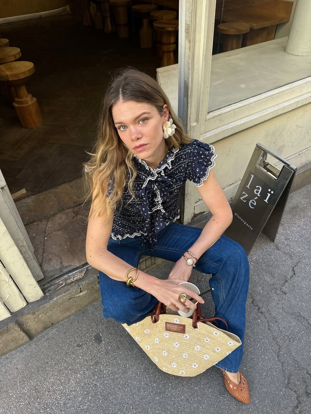 Foto de uma mulher loira usando um look composto por blusa azul, cal&ccedil;a jeans reta azul e bolsa de palha