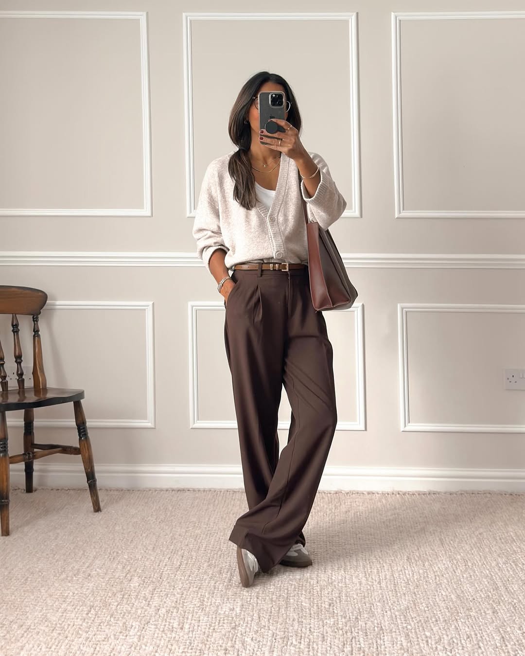 Foto de uma mulher morena usando um look composto por blusa de tric&ocirc;, cal&ccedil;a marrom e bolsa tamb&eacute;m marrom