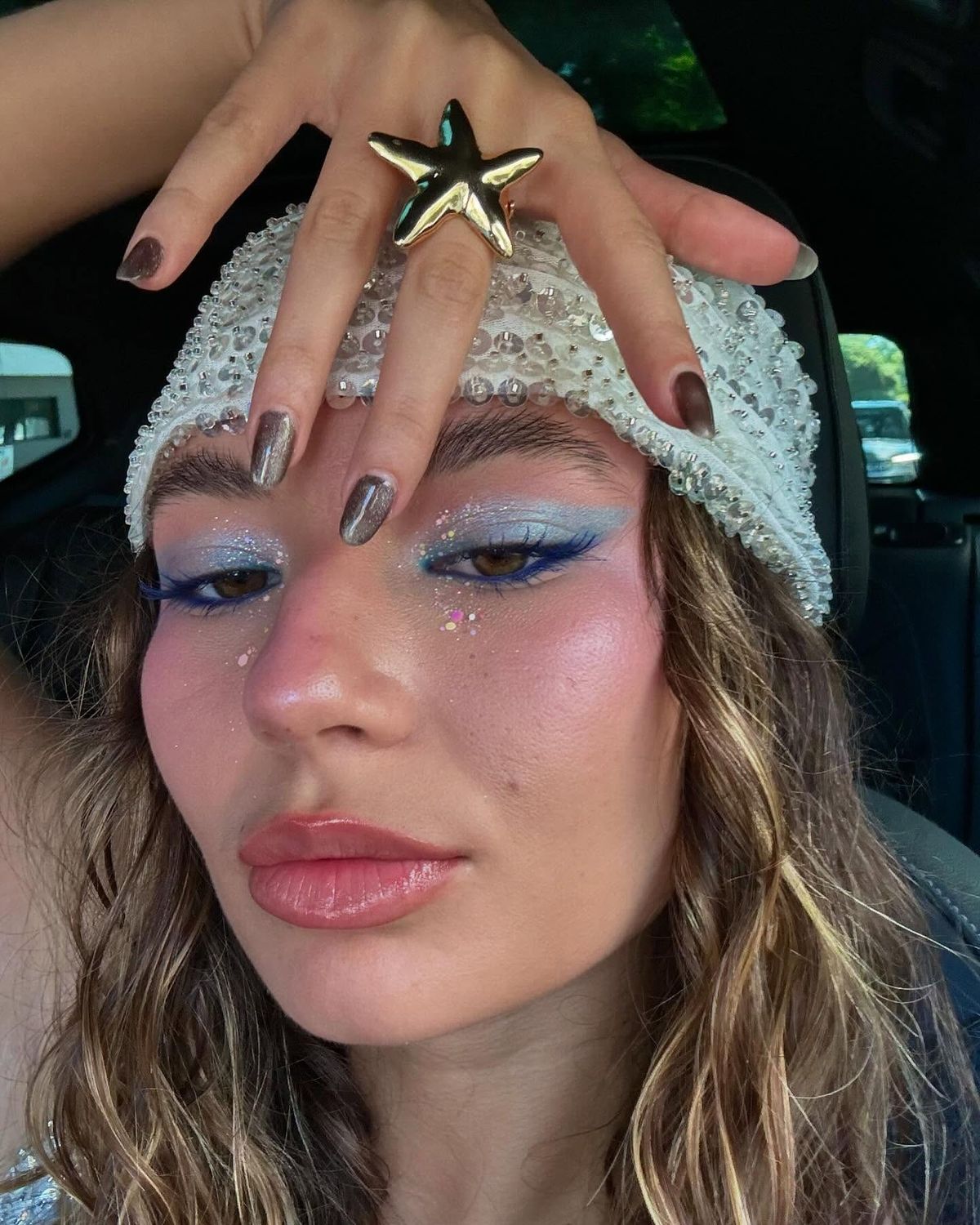 Mulher posando para selfie com maquiagem em tons de azul e rosa e touca no cabelo