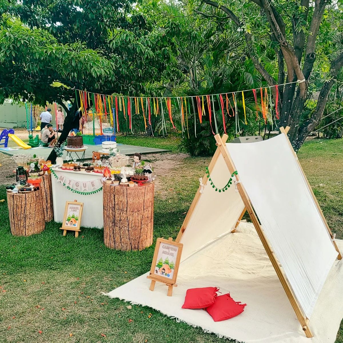 Mini acampamento no quintal montado com hastes de madeira, mesa de bolo e decora&ccedil;&atilde;o de anivers&aacute;rio
