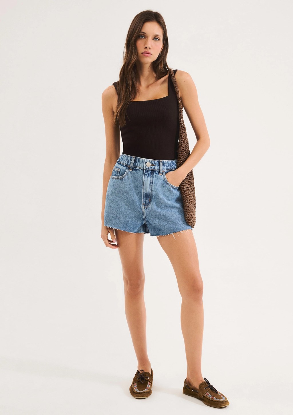 Foto de uma mulher morena usando um body preto e um short jeans