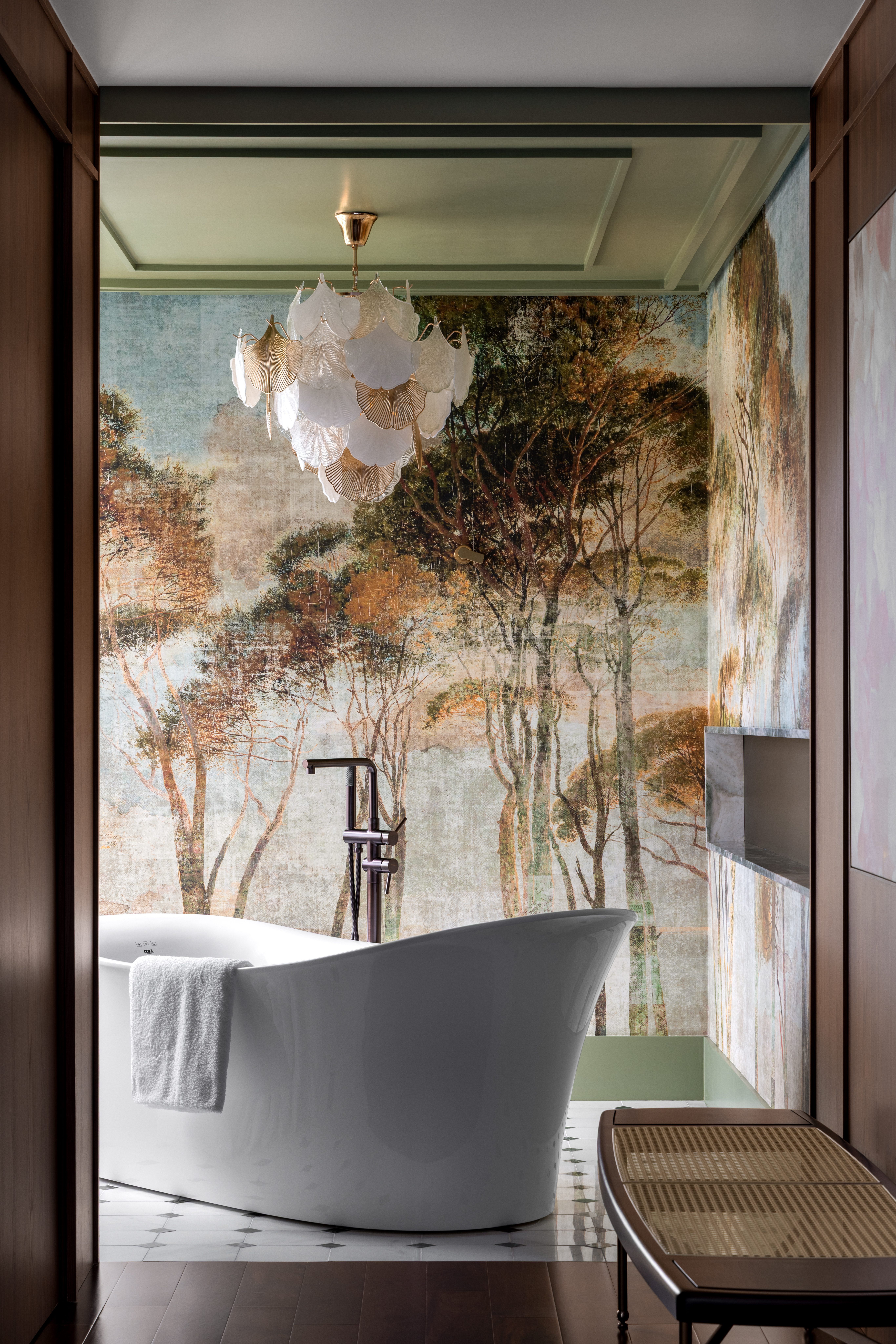 Banheiro com papel de parede de floresta, banheira branca, lustre e piso quadriculado