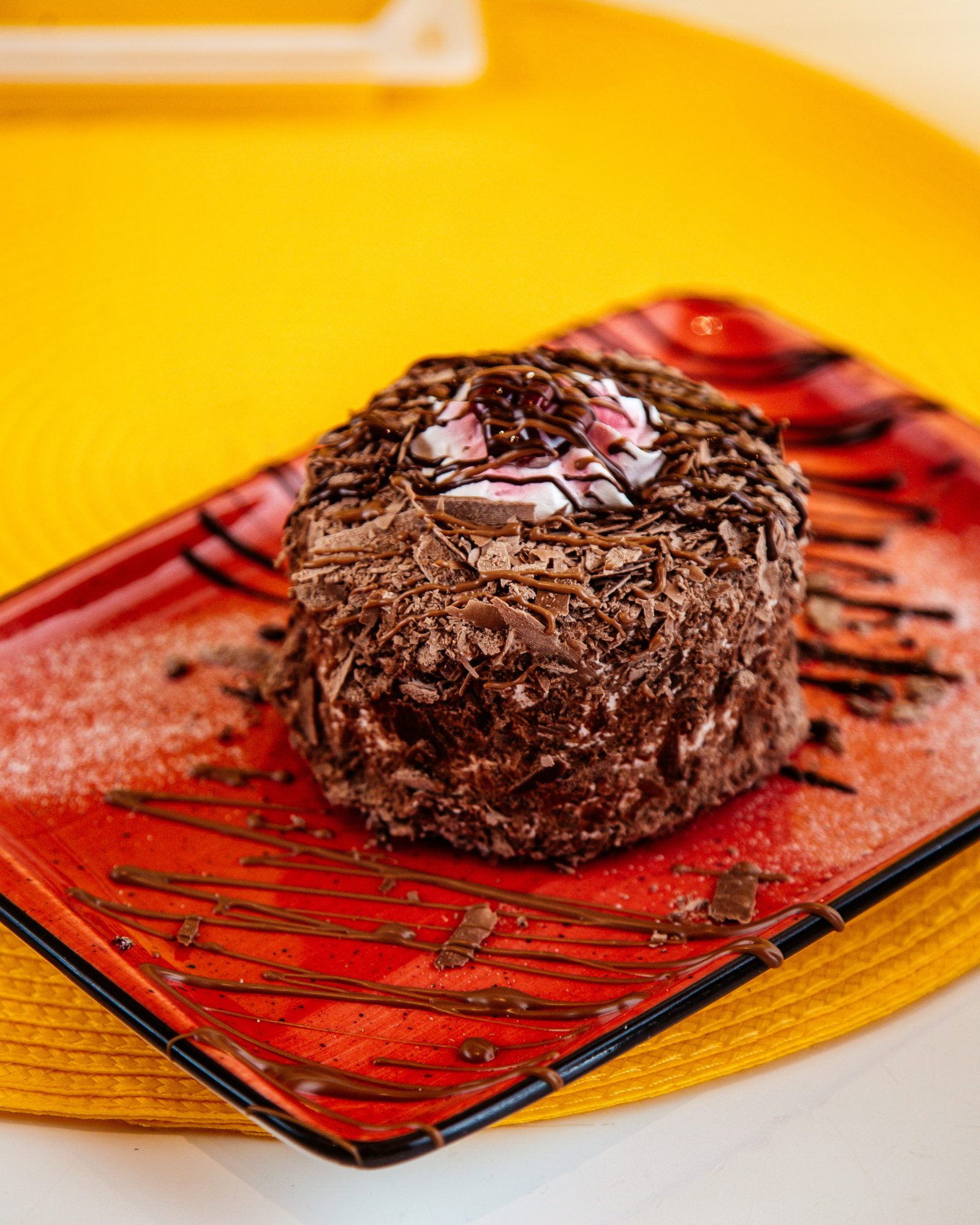 Imagem de brigadeir&atilde;o em um prato vermelho com mesa amarela ao fundo