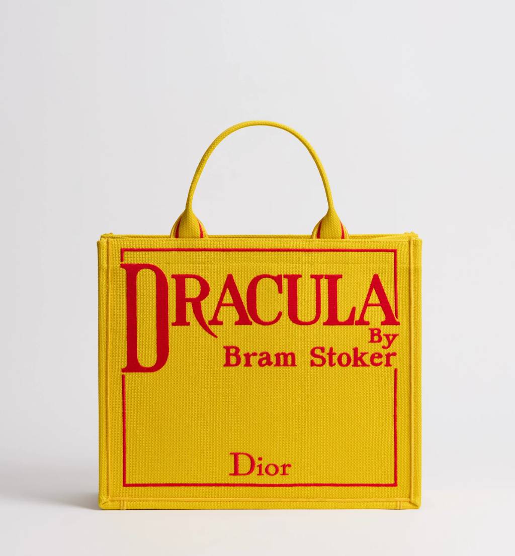 Dior Book Tote amarela com inscri&ccedil;&atilde;o vermelha &ldquo;Dracula by Bram Stoker&rdquo;, bolsa inspirada em romance g&oacute;tico cl&aacute;ssico, parte da cole&ccedil;&atilde;o liter&aacute;ria da Dior criada por Jonathan Anderson.