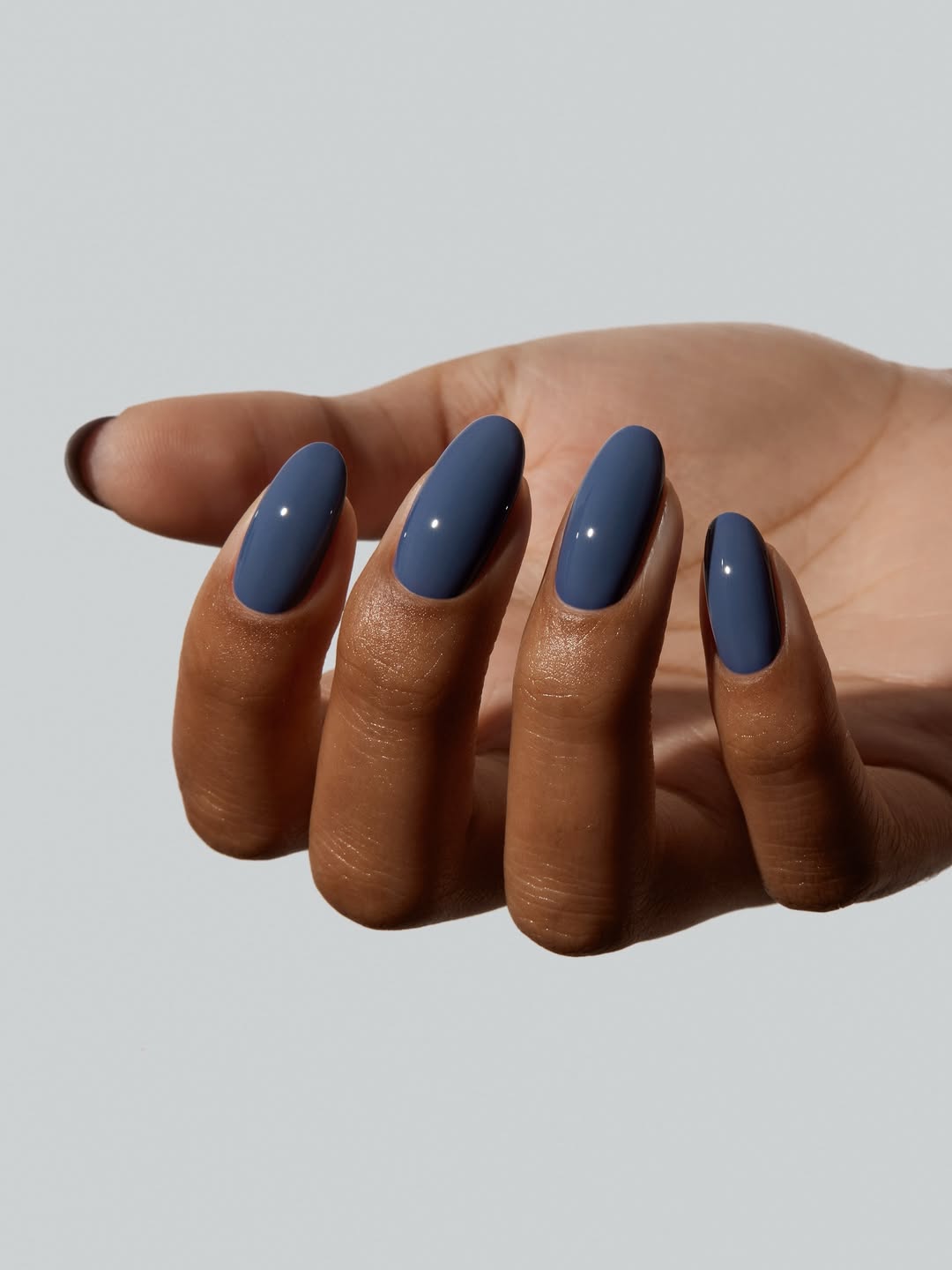 Esmalte azul escuro em unhas amendoadas destacando a pele negra