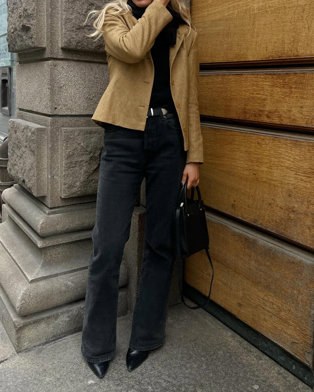 Foto de um look composto por cal&ccedil;a jeans preta, regra, cinto, blazer bege, bolsa preta e salto