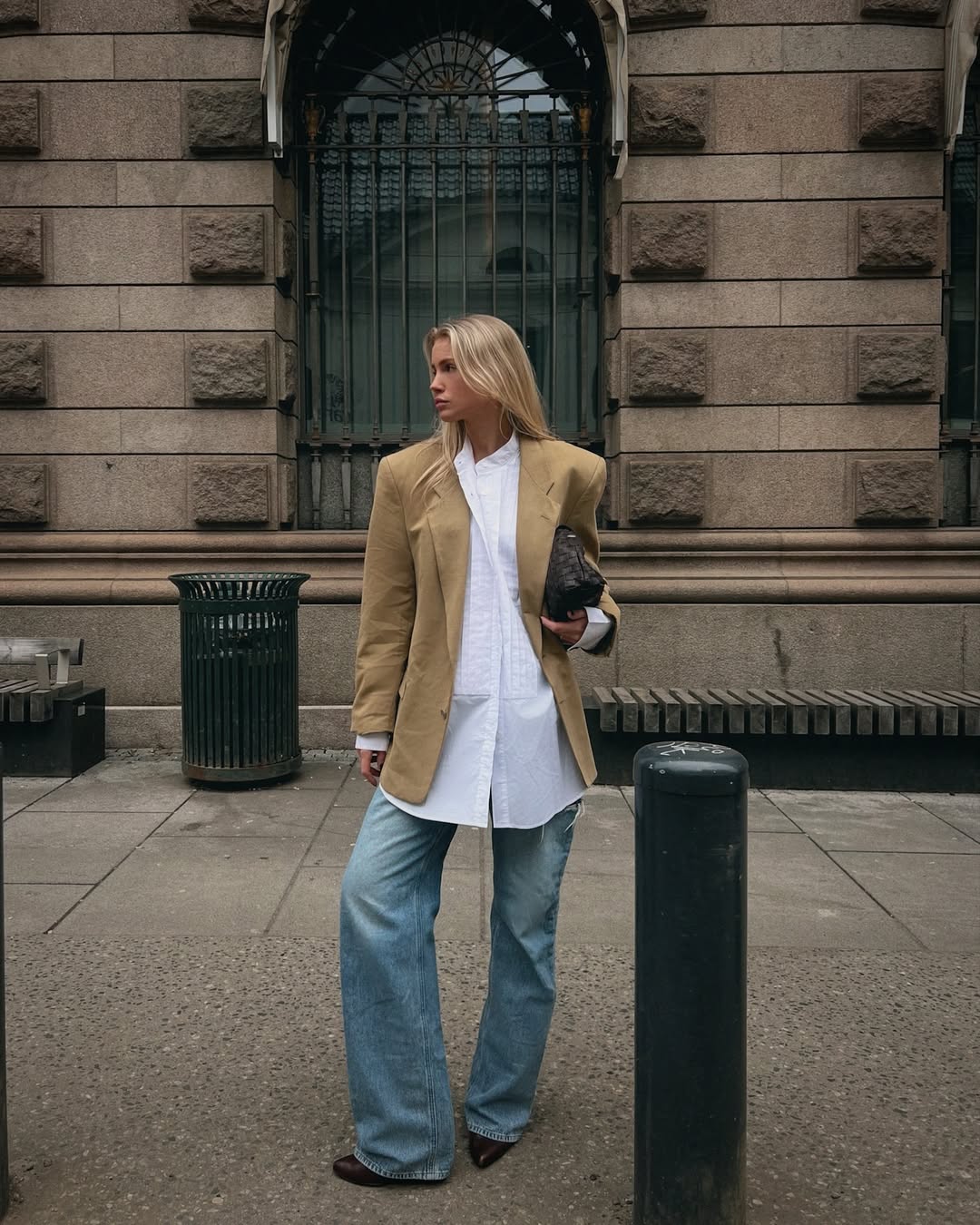 Foto de uma mulher loira usando um look composto por camisa branca oversized, blazer bege e cal&ccedil;a jeans