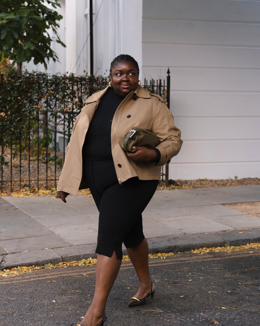 Foto de uma mulher negra com corpo plus size usando um look composto por camistea preta, cal&ccedil;a capri, blazer curto bege e salto
