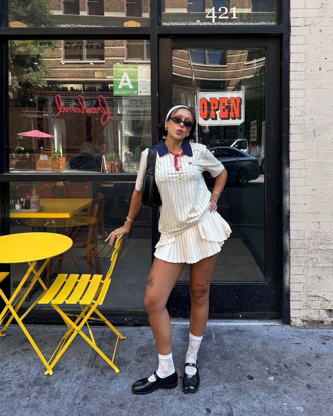 Foto de um look composto por blusa polo, saia plissada, meia branca e sapatilha preta