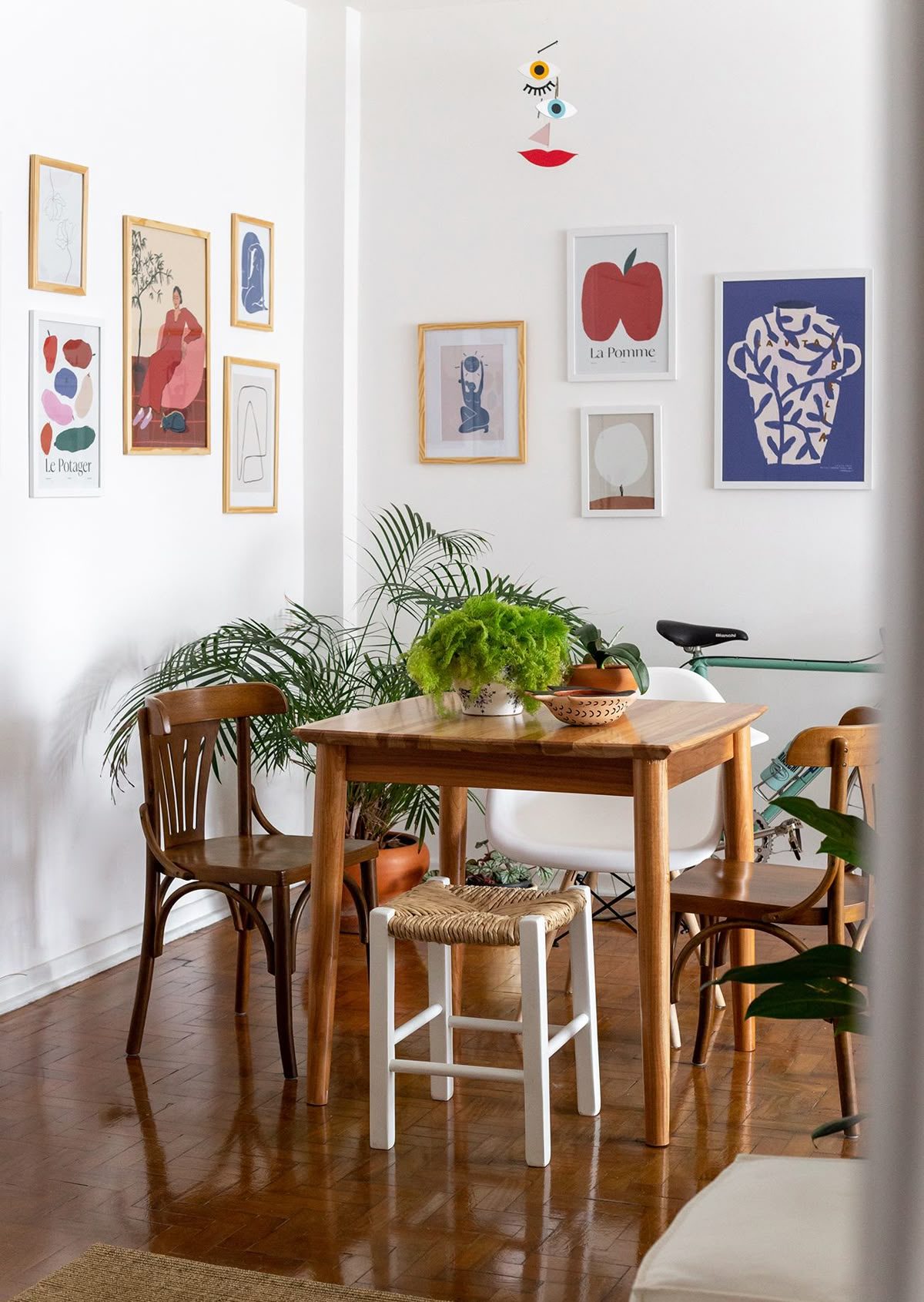 Sala de jantar com piso de madeira, quadros coloridos e com mesa quadrada