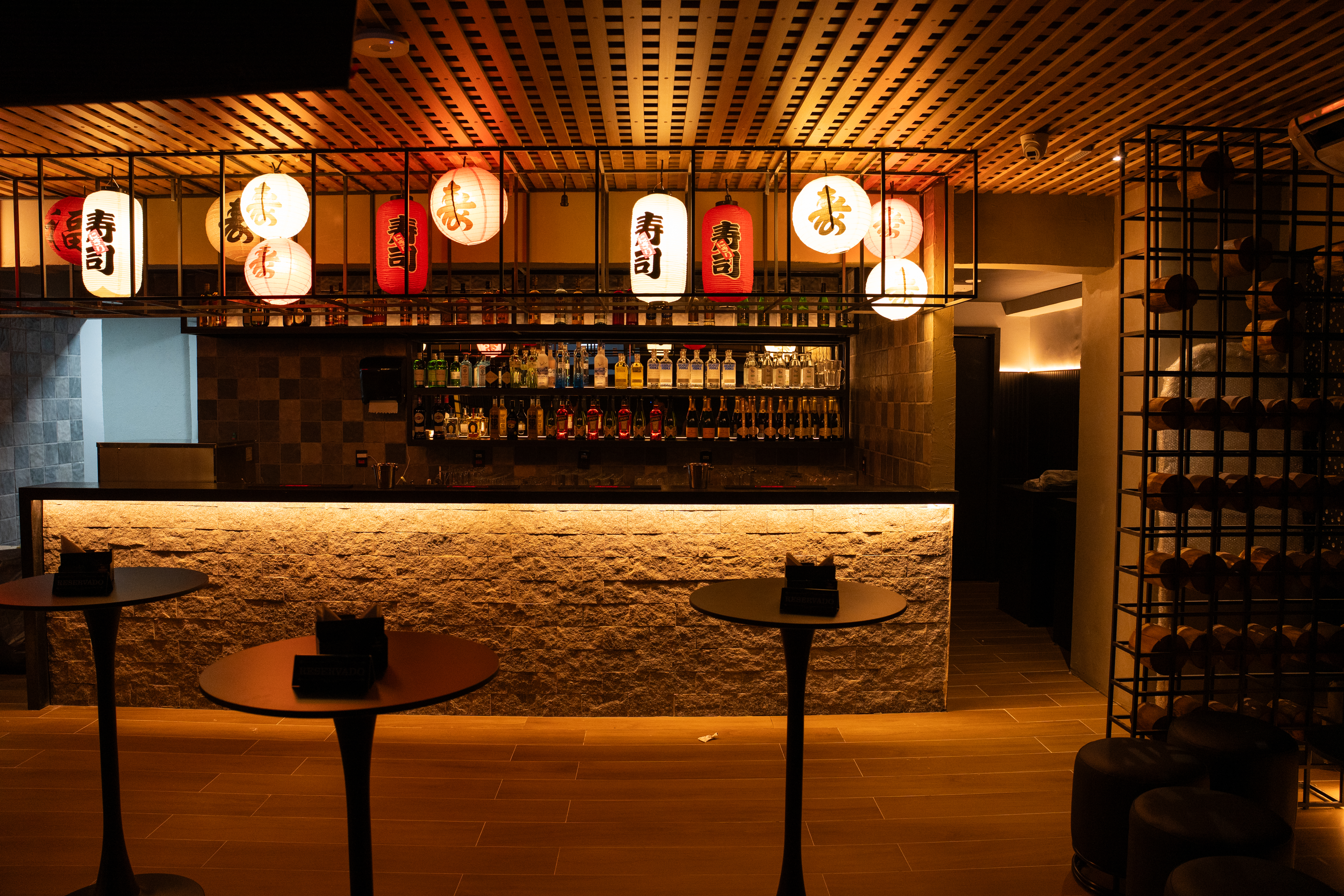 Bar da nova unidade do Yellow K em Pinheiros, S&atilde;o Paulo, com balc&atilde;o iluminado, garrafas expostas e lumin&aacute;rias orientais, espa&ccedil;o que integra a experi&ecirc;ncia de karaok&ecirc; com gastronomia chinesa e japonesa.