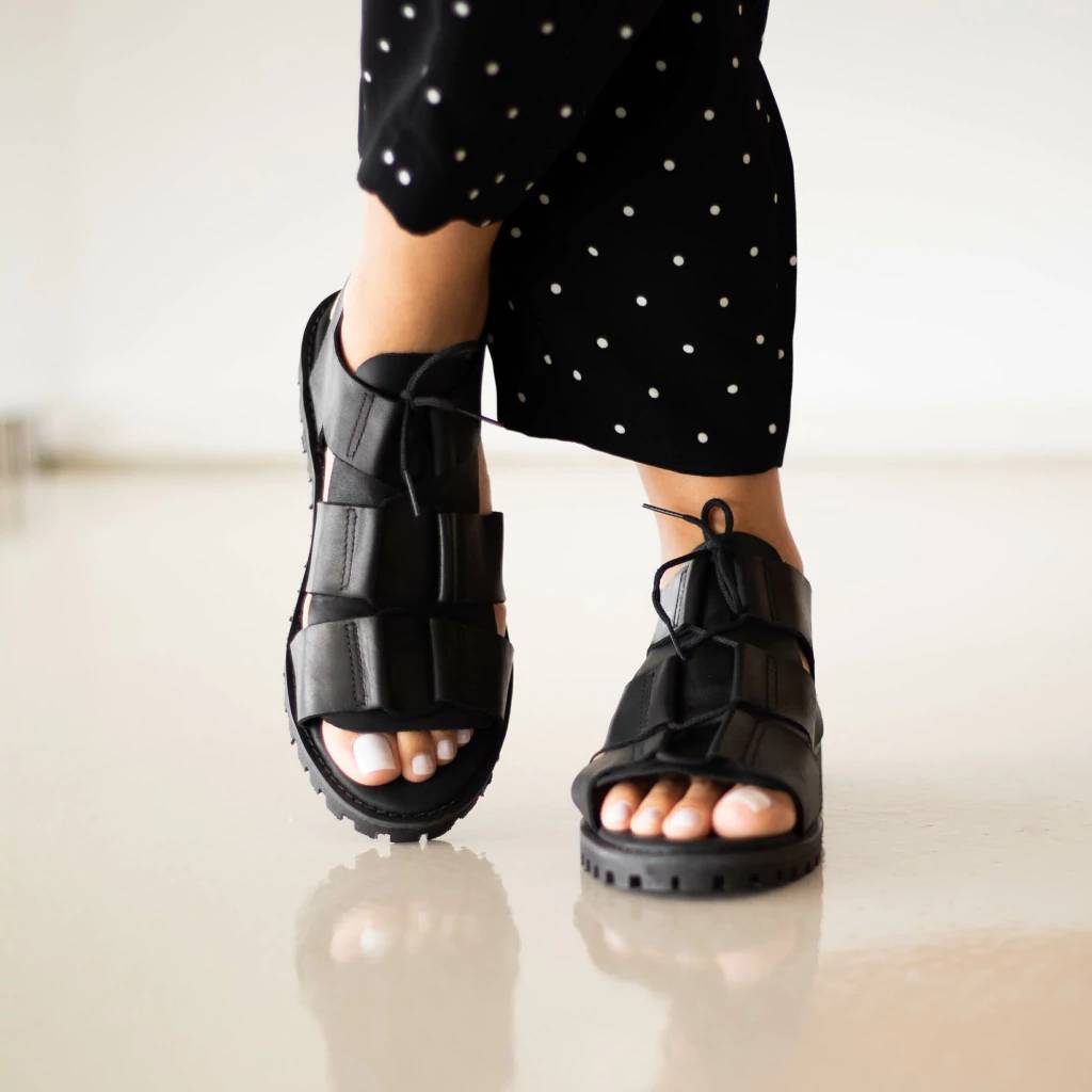 Mulher usando sand&aacute;lia de couro preto e cal&ccedil;a preta de po&aacute;