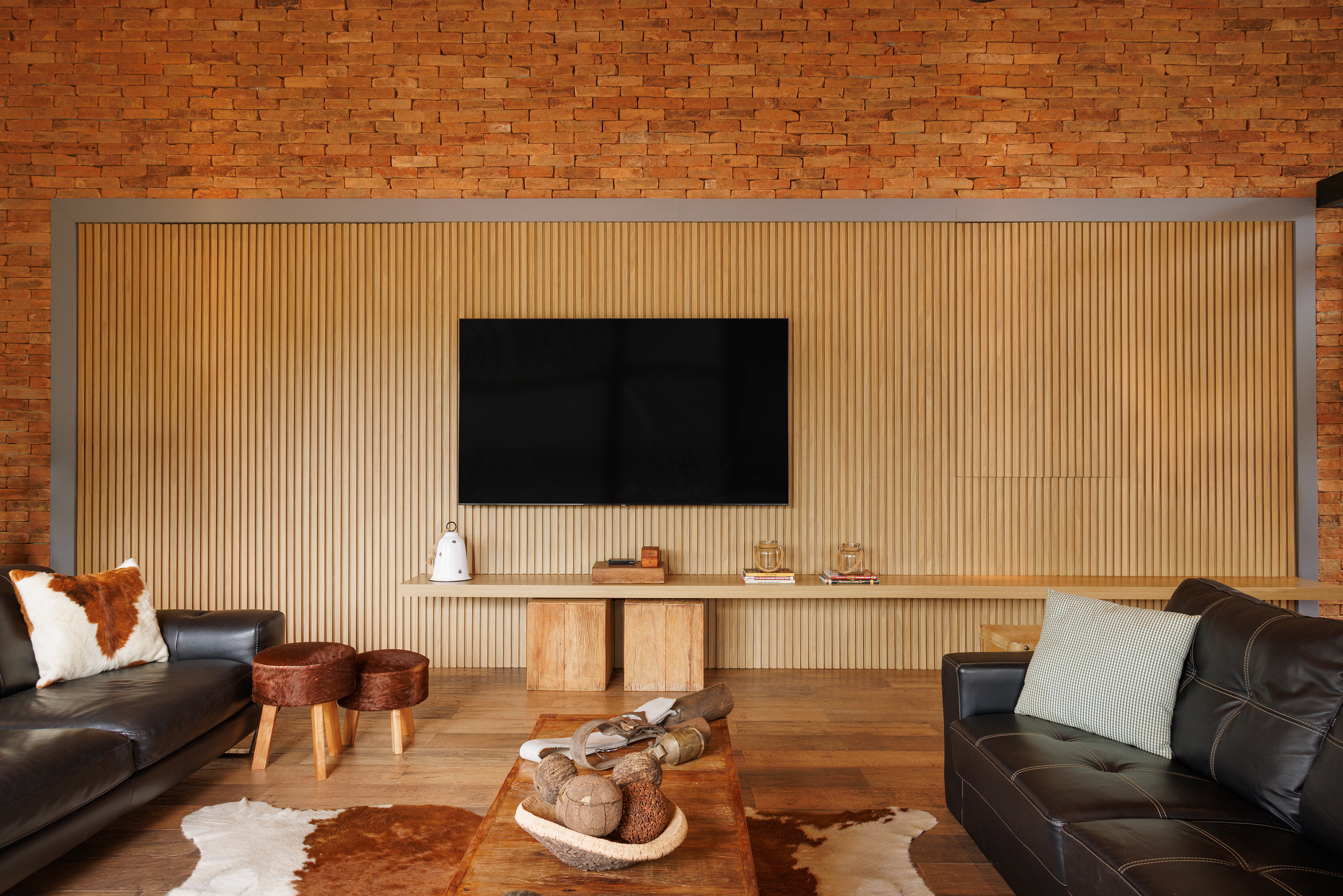 Sala de TV com parede de tijolos e painel ripado atr&aacute;s da tv