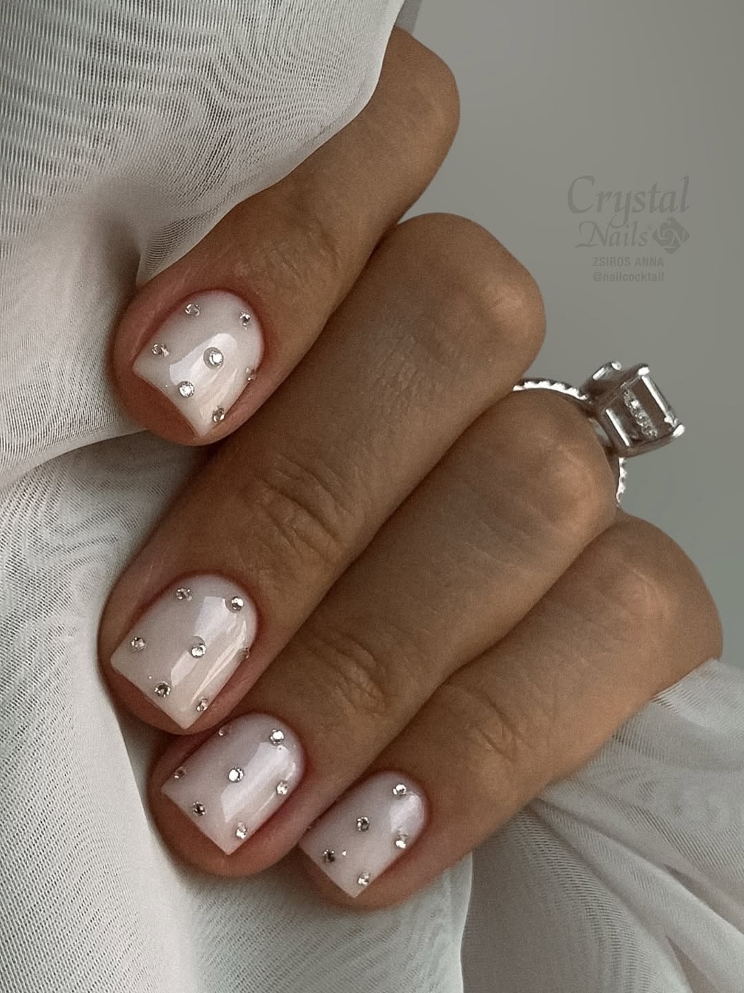 Unhas brancas decoradas com pequenas aplica&ccedil;&otilde;es de strass em base leitoso