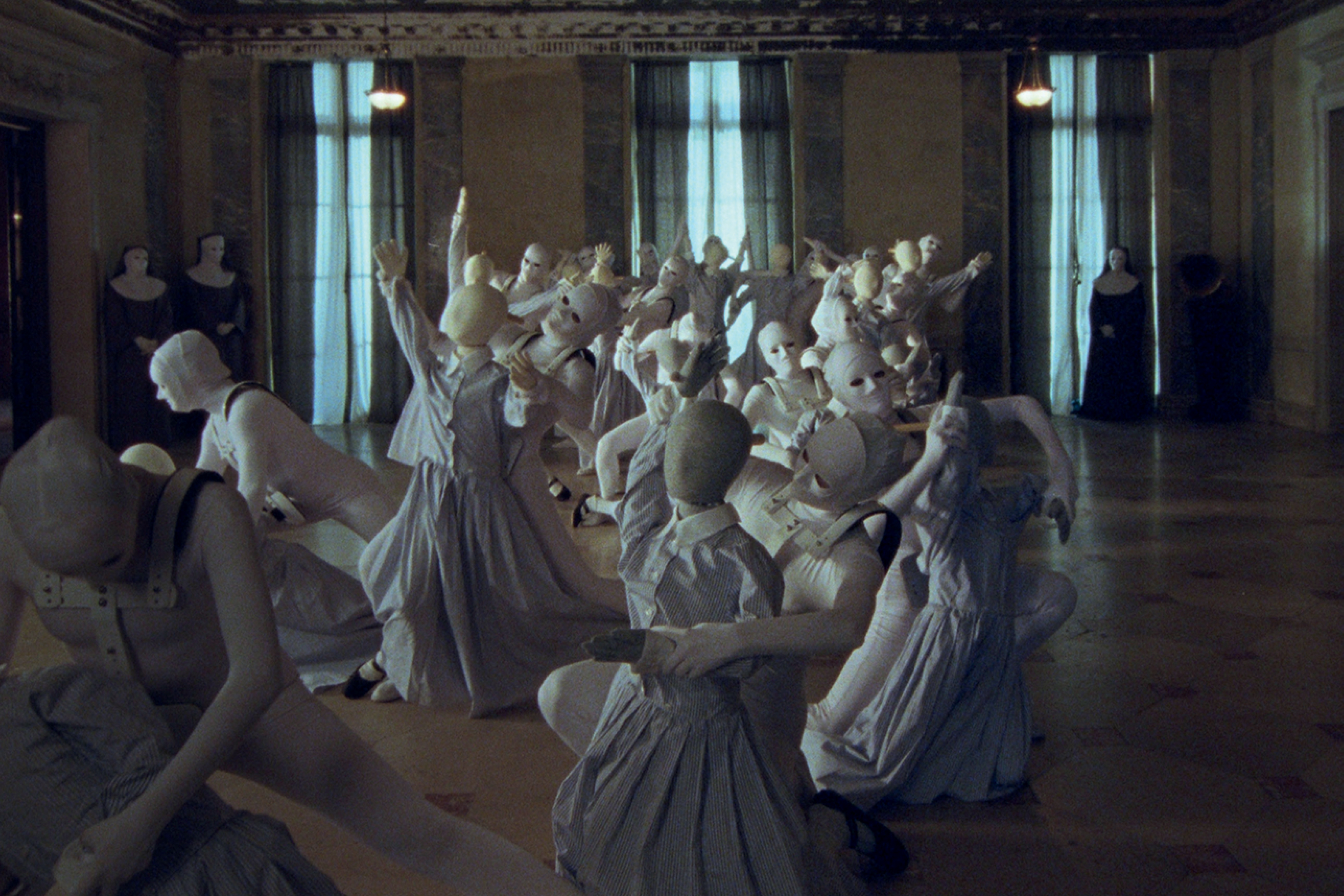 Cena do curta Discipline, do projeto Women&rsquo;s Tales, da Miu Miu. Em um ambiente austero, figuras vestidas de branco e usando m&aacute;scaras realizam uma coreografia enigm&aacute;tica, criando uma atmosfera surreal que mistura moda, cinema e performance.