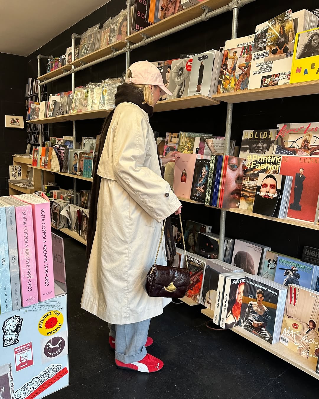 Mulher virada de costas em banca de jornal usando sobretudo branco e tenis vermelho