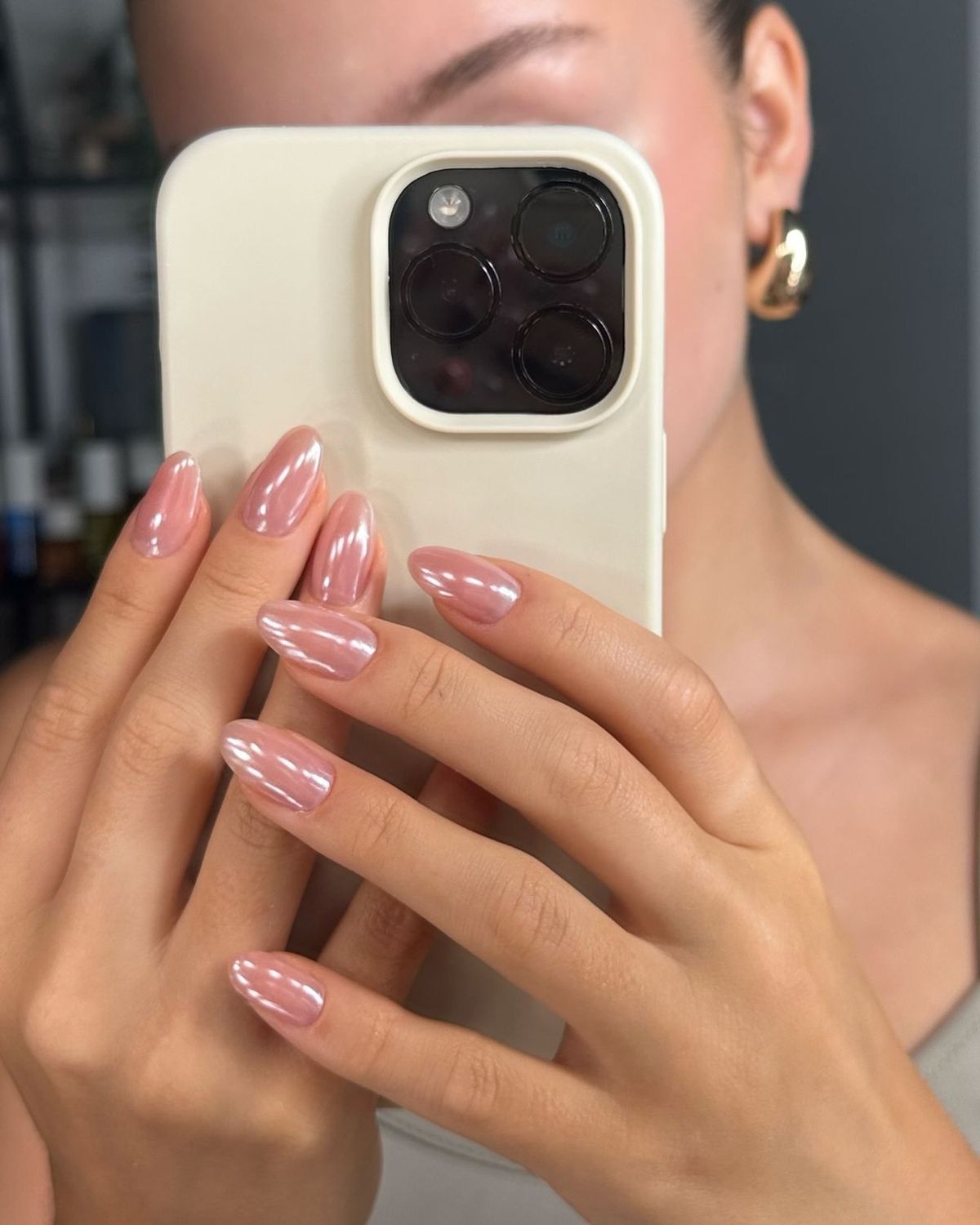 Mulher tirando foto no espelho com celular mostrando unhas pintadas de rosa beb&ecirc; espelhado