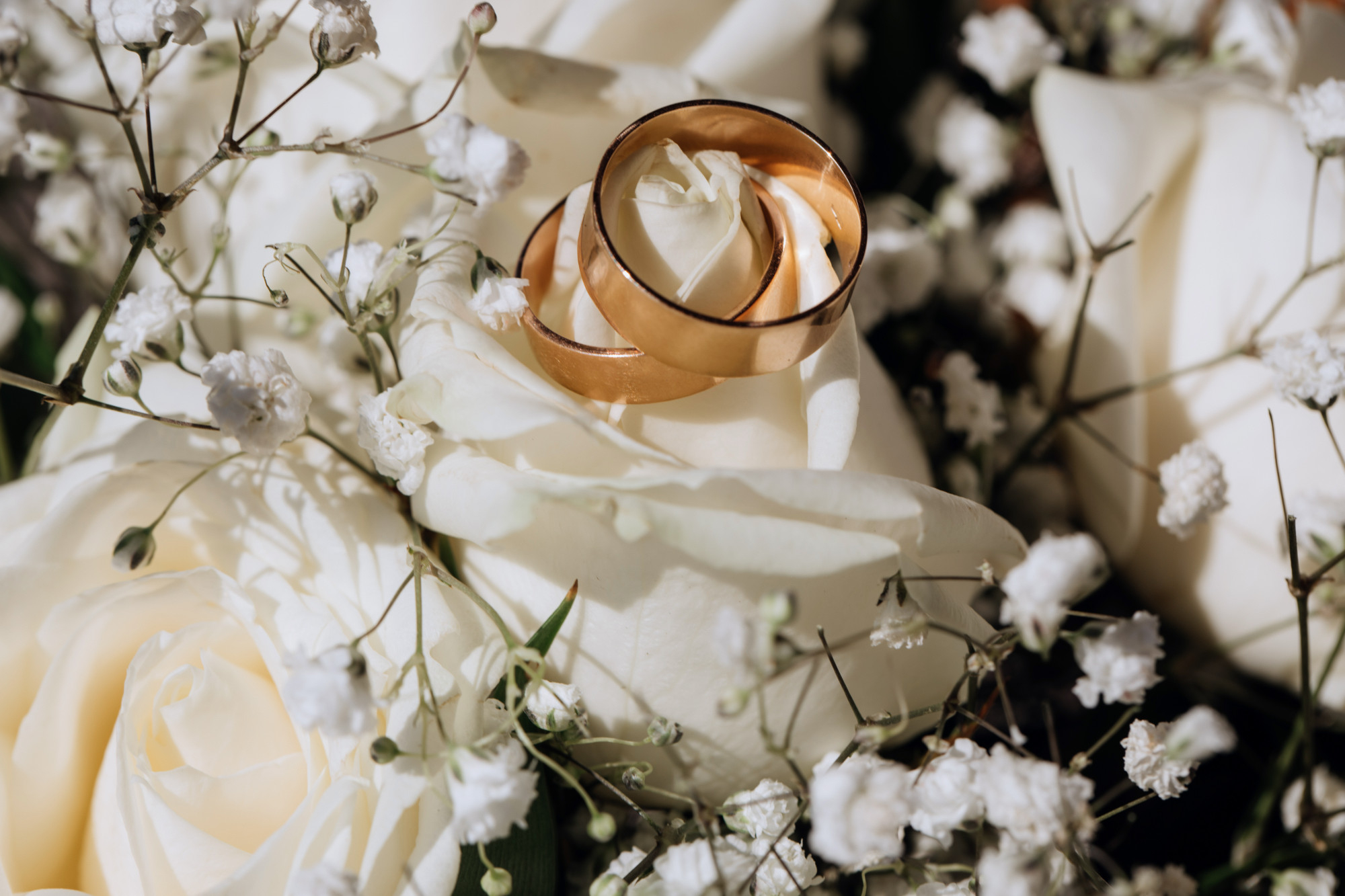 Alian&ccedil;as douradas apoiadas sobre flores brancas delicadas, em composi&ccedil;&atilde;o rom&acirc;ntica de casamento.