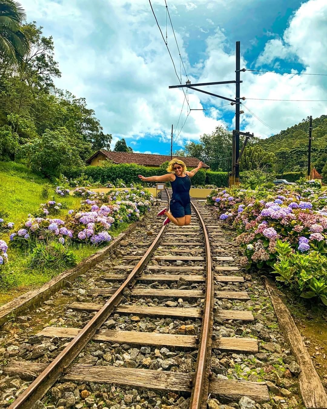 Visitante salta sobre trilhos da esta&ccedil;&atilde;o ferrovi&aacute;ria Eug&ecirc;nio Lefevre, cercada por hort&ecirc;nsias e natureza em Santo Ant&ocirc;nio do Pinhal.