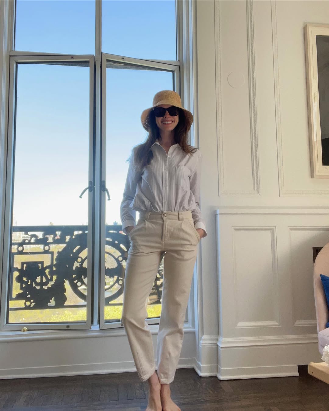 Foto de Anne Hathaway usando um look composto por camisa branca, cal&ccedil;a bege e chap&eacute;u de palha