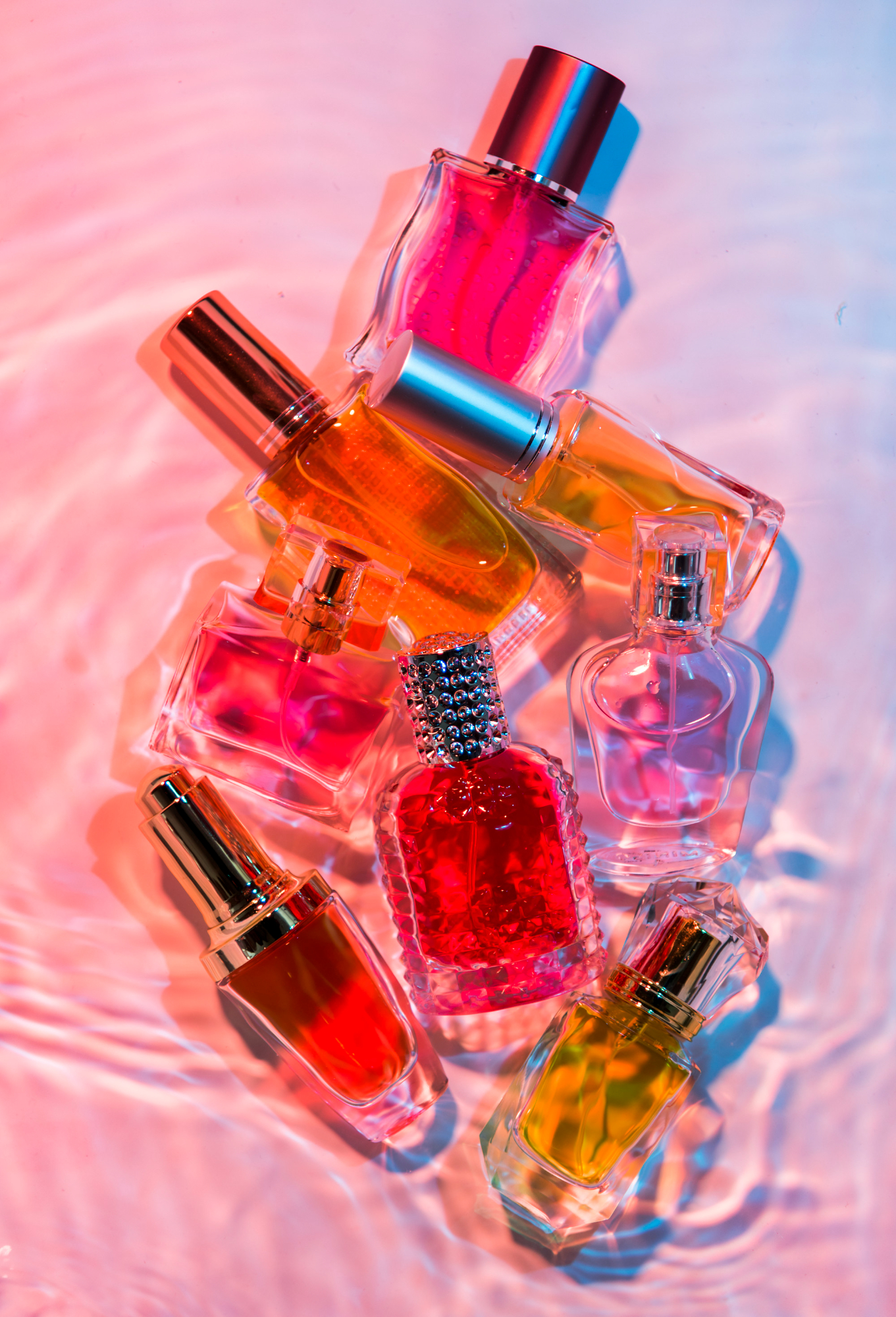 Conjunto de frascos de perfume coloridos sobre superf&iacute;cie iluminada, representando a personaliza&ccedil;&atilde;o de fragr&acirc;ncias no universo do DIY.