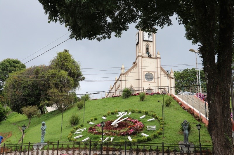 Rel&oacute;gio de flores em Santo Ant&ocirc;nio do Pinhal com igreja ao fundo, um dos pontos tur&iacute;sticos mais fotografados do centro da cidade.