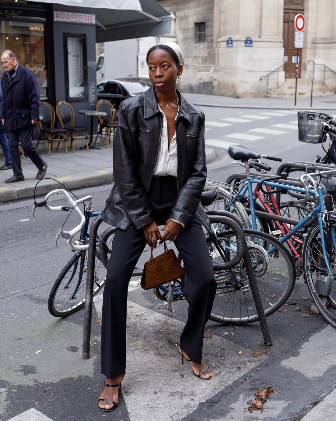 Foto de uma mulher negra usando um look composto por jaquea de couro, cala jeans prera, bolsaa vinho e salto