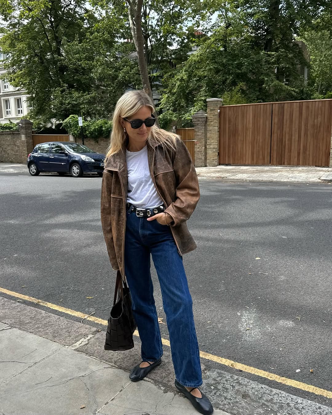 Foto de uma mulher loira usando um look composto por jaqueta marrom, camiseta branca, cal&ccedil;a jeans reta, bolsa e sapatilha