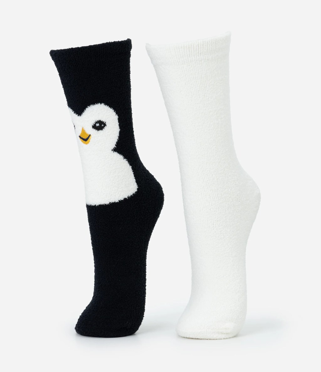 Par de meias de pel&uacute;cia, uma preta com rosto de pinguim branco e bico amarelo, e outra branca lisa, ambas em fundo claro