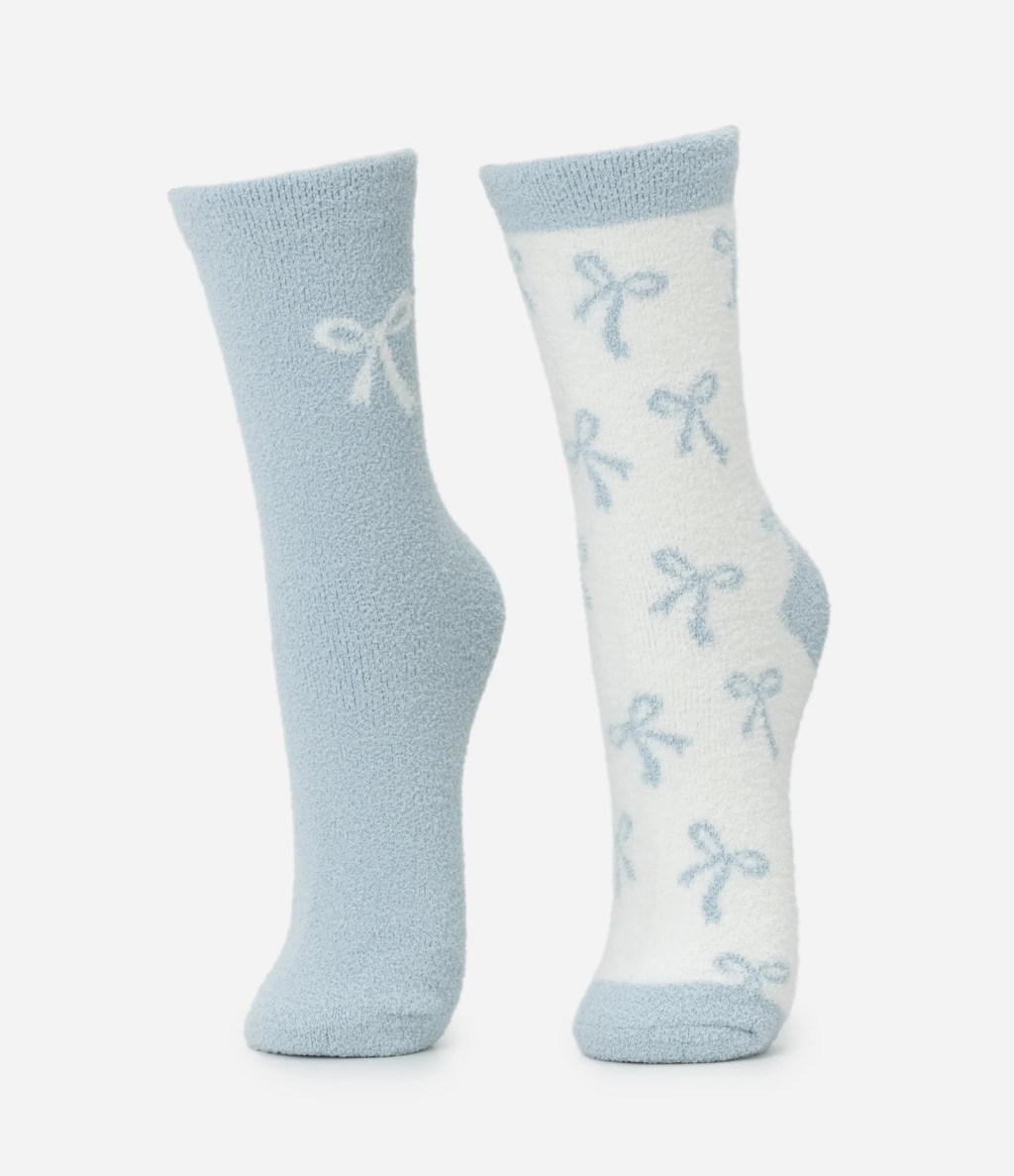 Par de meias de plush azul claro e branco. A meia esquerda &eacute; azul clara com um la&ccedil;o branco. A meia direita &eacute; branca com v&aacute;rios la&ccedil;os azuis claros e detalhes azuis no calcanhar e ponta