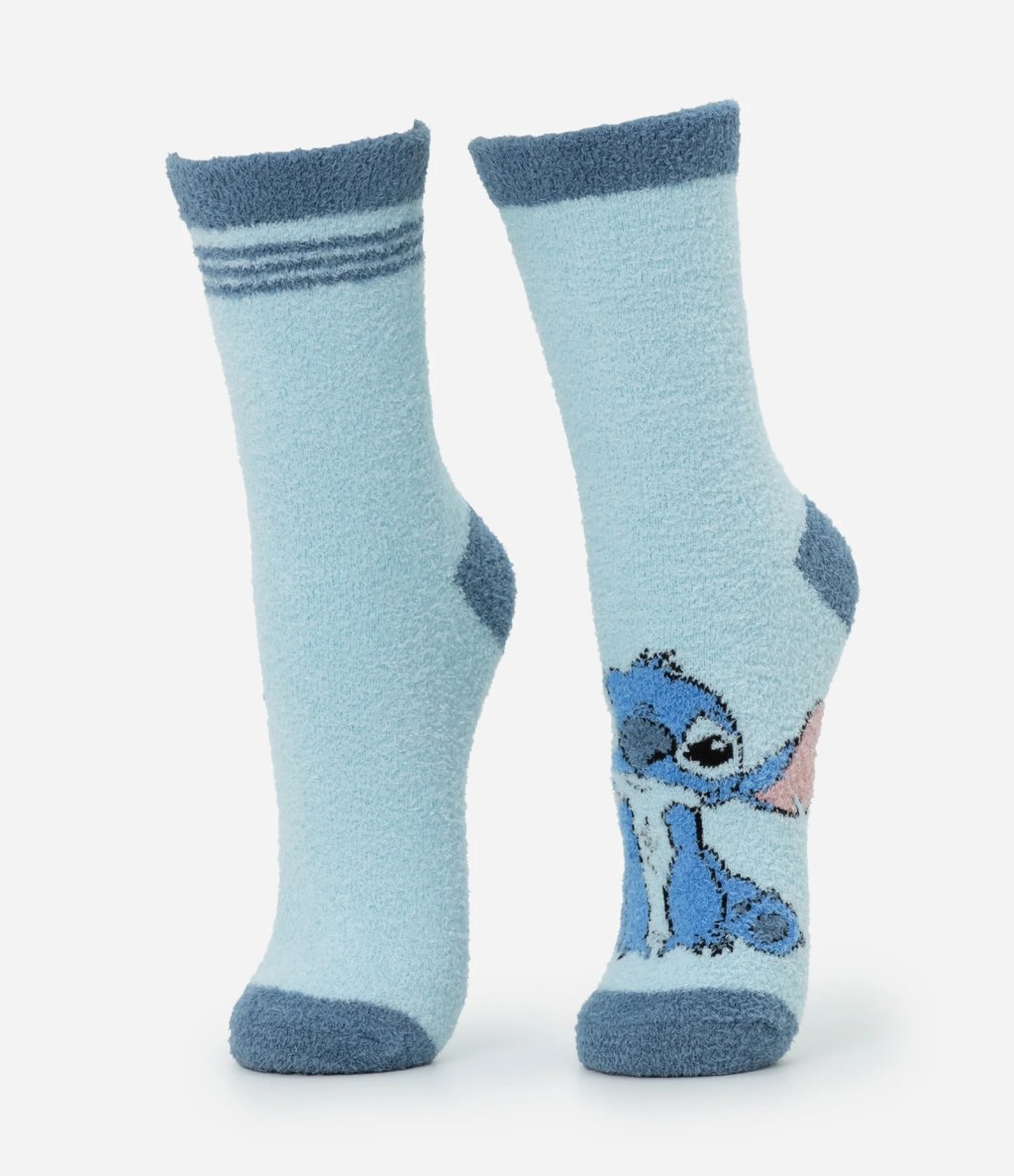 Par de meias de plush azul-claro com detalhes azul-marinho. A meia esquerda tem tr&ecirc;s listras horizontais no punho. A meia direita exibe o personagem Stitch, de Lilo & Stitch, sentado, com orelhas rosadas, na parte frontal