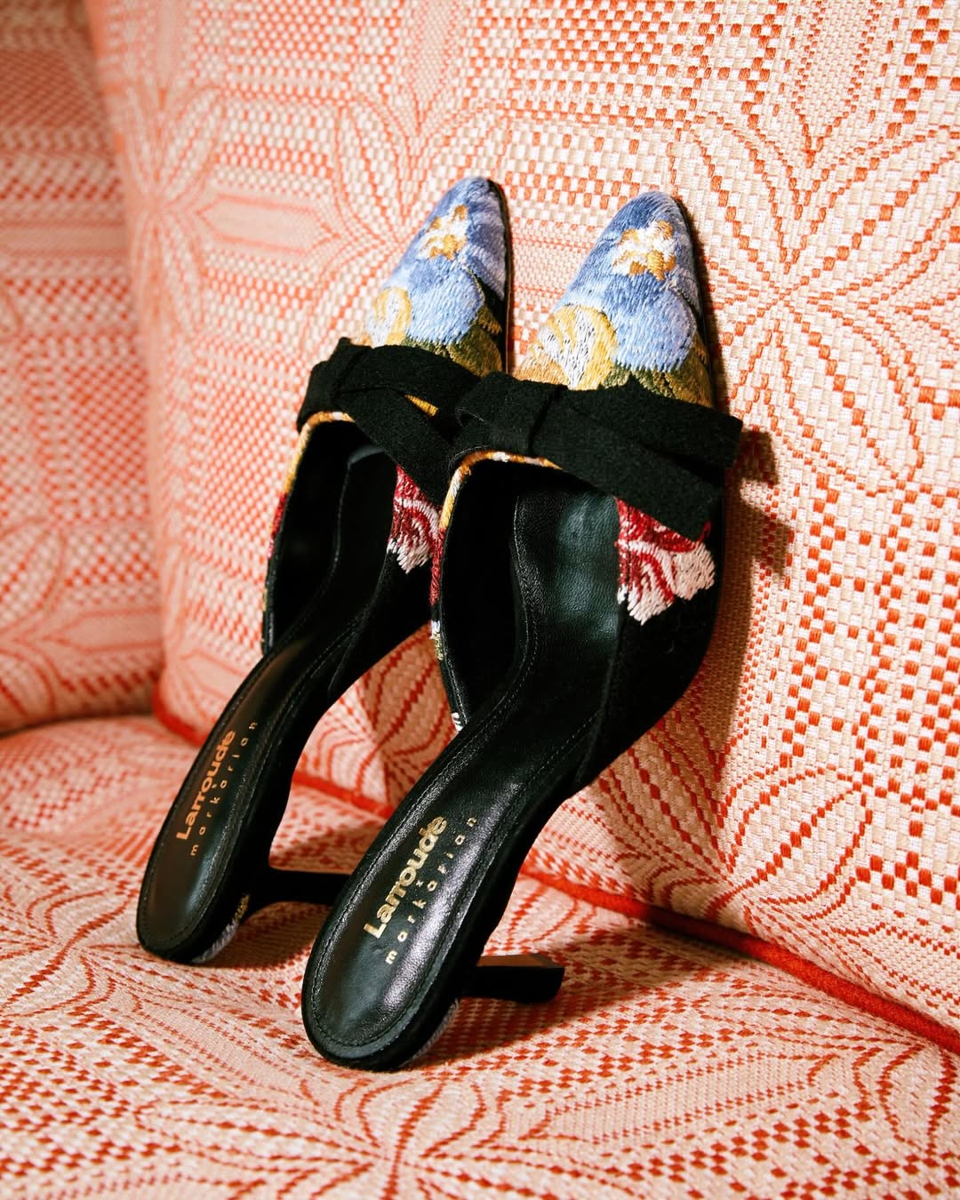 Foto de um mule preto, com estampa na parte frontal, apoiado em um sof&aacute; vermelho e branco