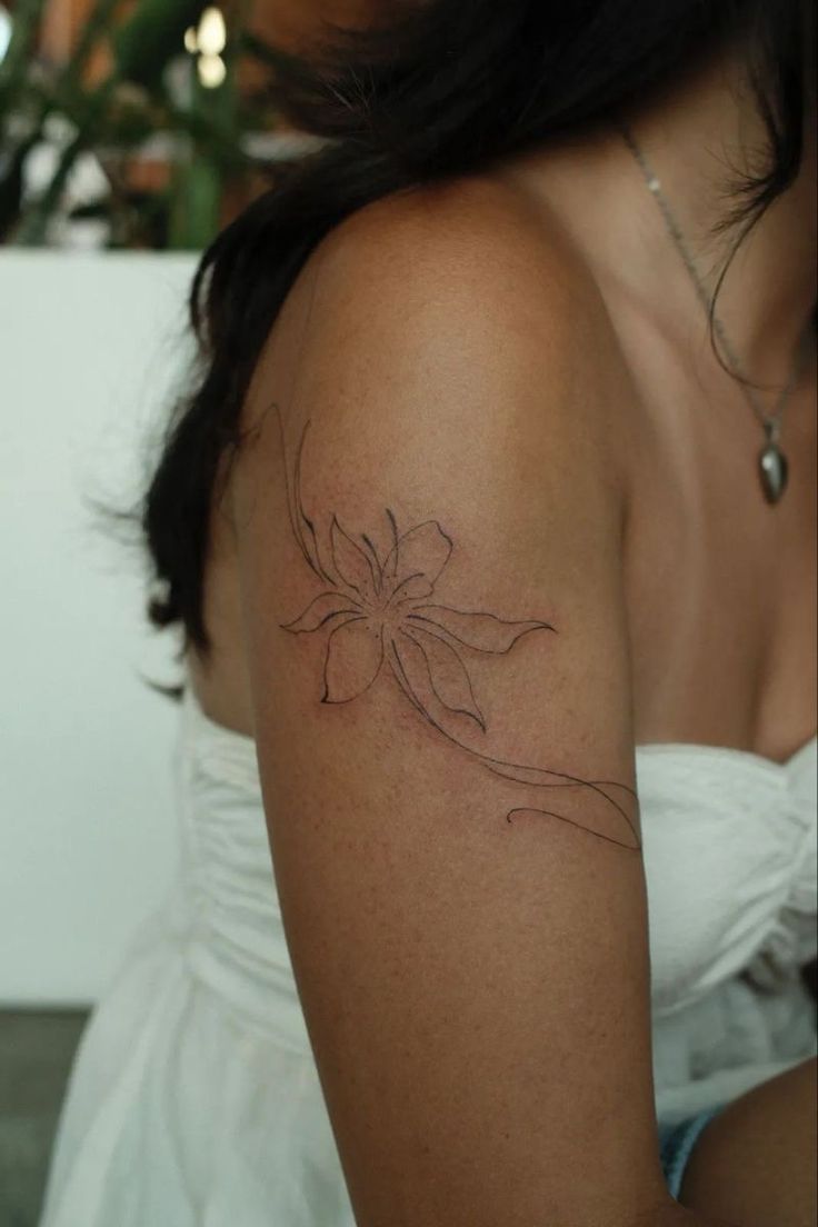 Tatuagem de flor em fine line no ombro, com tra&ccedil;o livre que d&aacute; sensa&ccedil;&atilde;o de movimento e muita eleg&acirc;ncia