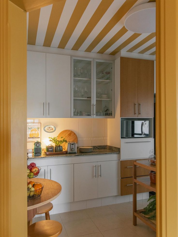 Teto listrado em amarelo e branco emoldurando cozinha com arm&aacute;rios brancos