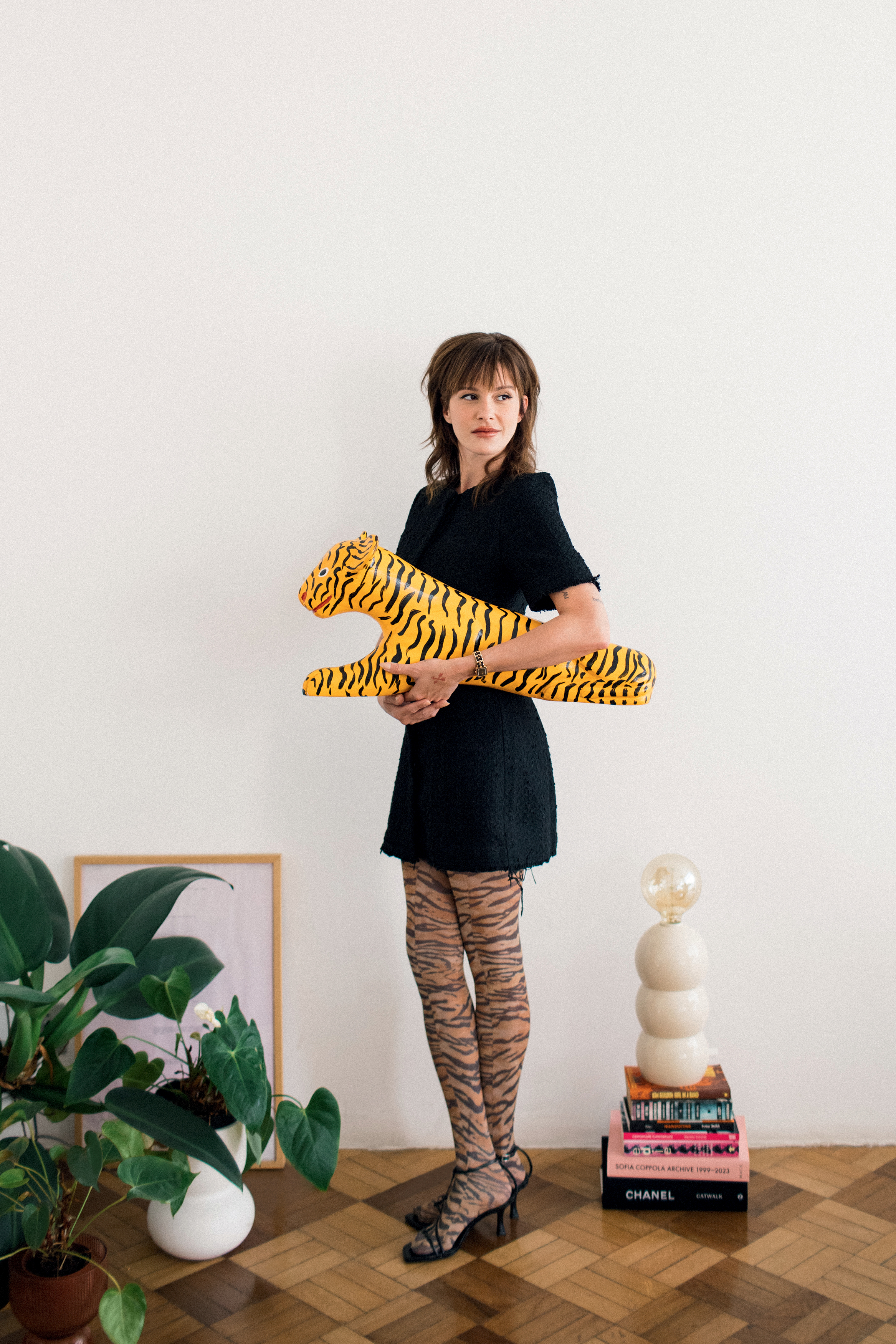 Foto de Verena Figueiredo. Nela, ela aparece usando um vestido preto, uma legging de tigre e um salto preto. Al&eacute;m disso, ela segura no bra&ccedil;o um objeto de decora&ccedil;&atilde;o que imita um tigre