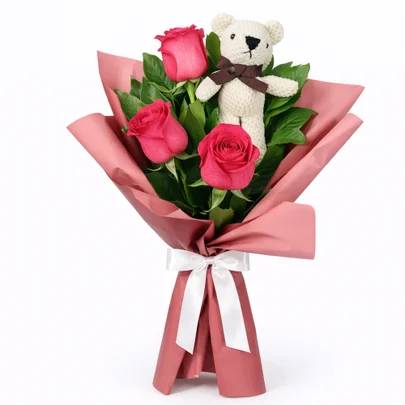 Buqu&ecirc; com tr&ecirc;s rosas cor-de-rosa, folhas verdes e um ursinho de pel&uacute;cia branco com la&ccedil;o marrom, envolto em papel rosa e amarrado com fita branca