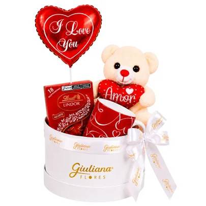 Cesta de presente branca com la&ccedil;o, contendo um bal&atilde;o vermelho em formato de cora&ccedil;&atilde;o com I Love You, uma caixa de chocolates Lindt, uma caneca vermelha com cora&ccedil;&otilde;es brancos e um ursinho de pel&uacute;cia bege segurando um cora&ccedil;&atilde;o vermelho com Amor