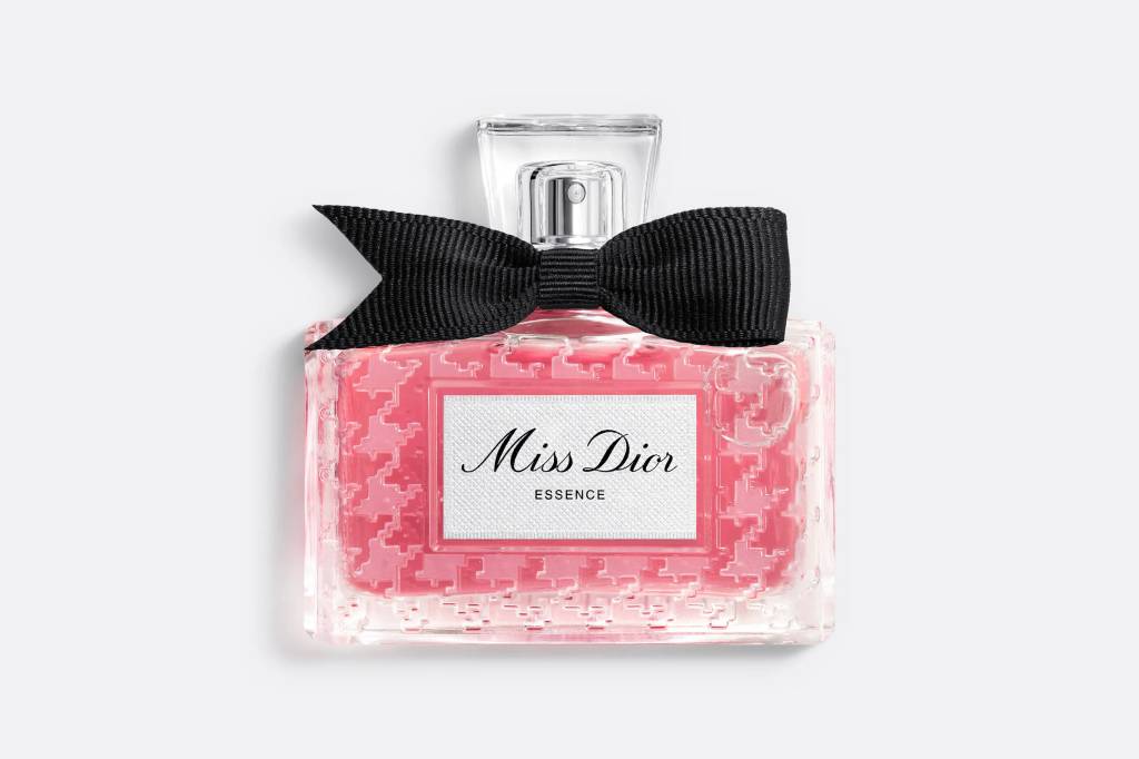 Frasco retangular de perfume Miss Dior Essence, com l&iacute;quido rosa claro e padr&atilde;o houndstooth em relevo, tampa transparente e la&ccedil;o preto de gorgor&atilde;o no gargalo
