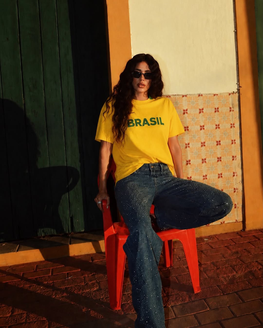 Mulher de cabelos longos e escuros, &oacute;culos escuros, camiseta amarela com 