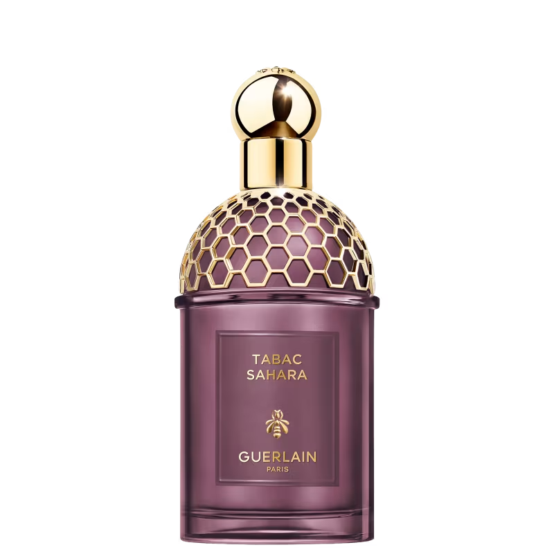 Frasco de perfume Guerlain Tabac Sahara em vidro roxo transl&uacute;cido, com tampa dourada em formato de c&uacute;pula com padr&atilde;o de colmeia e um borrifador dourado. O r&oacute;tulo retangular no centro do frasco exibe TABAC SAHARA, uma abelha e GUERLAIN PARIS em dourado