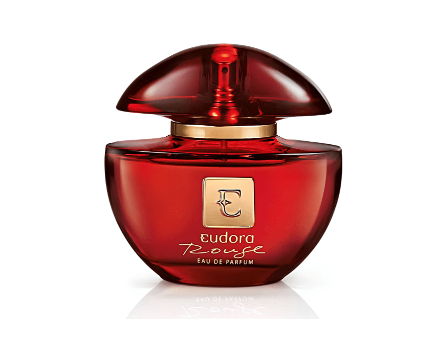 Frasco de perfume Eudora Rouge Eau de Parfum vermelho-rubi com tampa em formato de c&uacute;pula e detalhes dourados, refletido na superf&iacute;cie branca