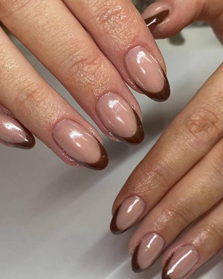 M&atilde;os femininas com unhas ovais, esmalte nude e pontas em francesinha marrom-escuro, exibindo um design moderno e elegante