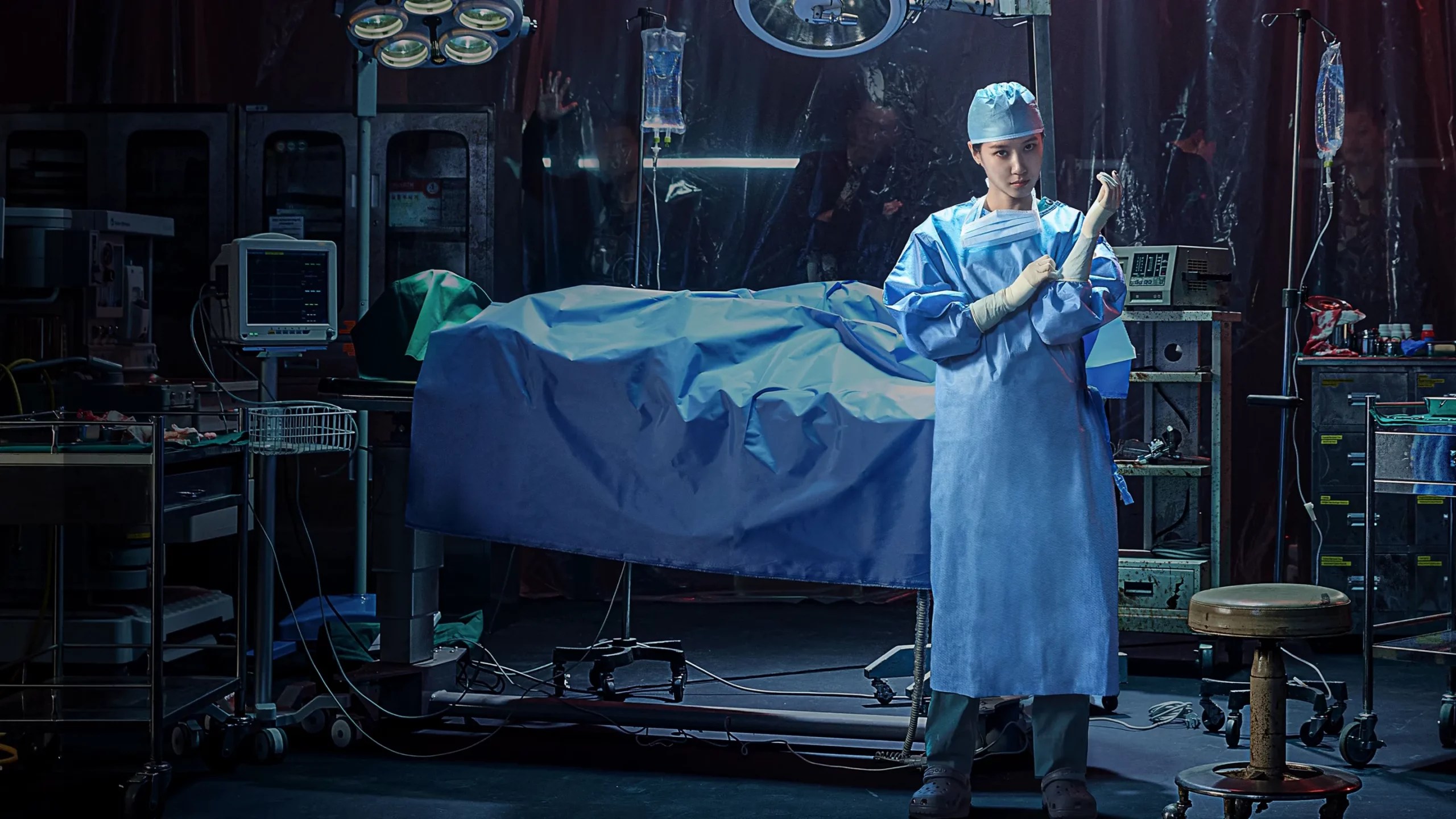 Uma médica asiática, vestindo uniforme cirúrgico azul e touca, coloca luvas em uma sala de cirurgia escura e bagunçada, com uma maca coberta por um lençol azul e equipamentos médicos ao redor
