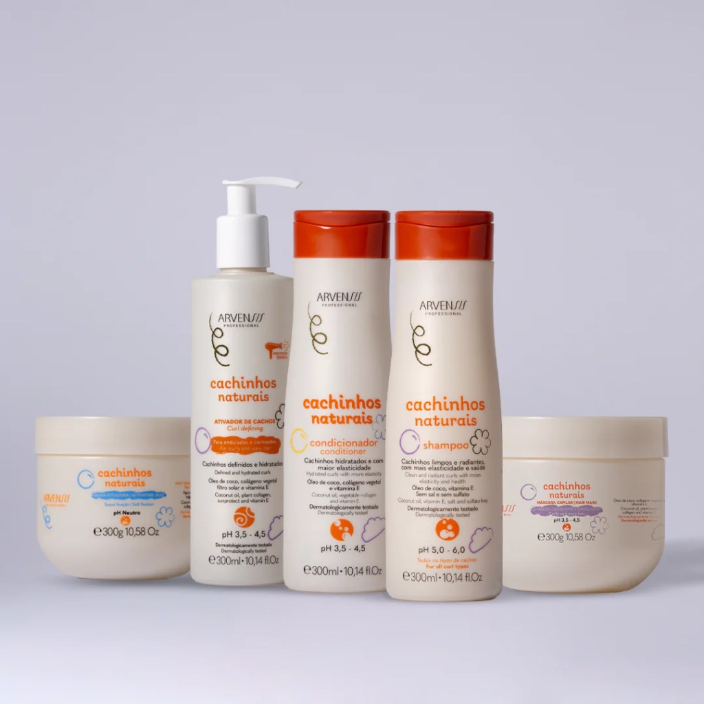 Cinco produtos Arvensis Cachinhos Naturais para cabelos cacheados: ativador de cachos, condicionador, shampoo e duas m&aacute;scaras capilares, em embalagens brancas com detalhes laranja e roxos, sobre fundo claro