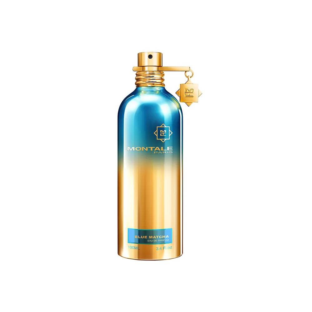Frasco de perfume Montale Paris Blue Matcha, cil&iacute;ndrico, com gradiente de azul met&aacute;lico na parte superior e dourado na inferior. Possui borrifador dourado e um pingente dourado com o monograma M pendurado no gargalo. Um r&oacute;tulo azul na base indica BLUE MATCHA EAU DE PARFUM 100ML 3.4 FL.OZ
