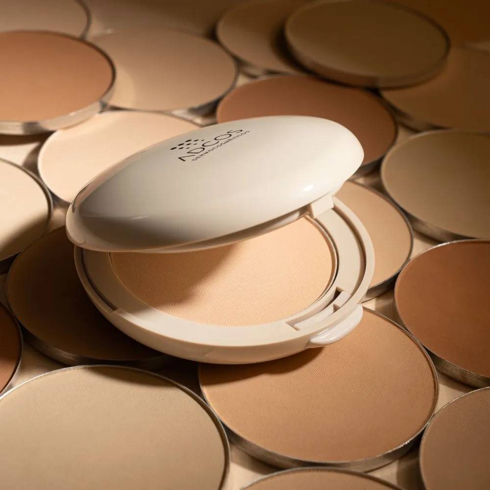 Um p&oacute; compacto bege claro aberto, com a tampa branca exibindo o logo NEOS DERMOCOSM&Eacute;TICOS, cercado por diversos refis de p&oacute; compacto em tons de pele variados, do claro ao escuro