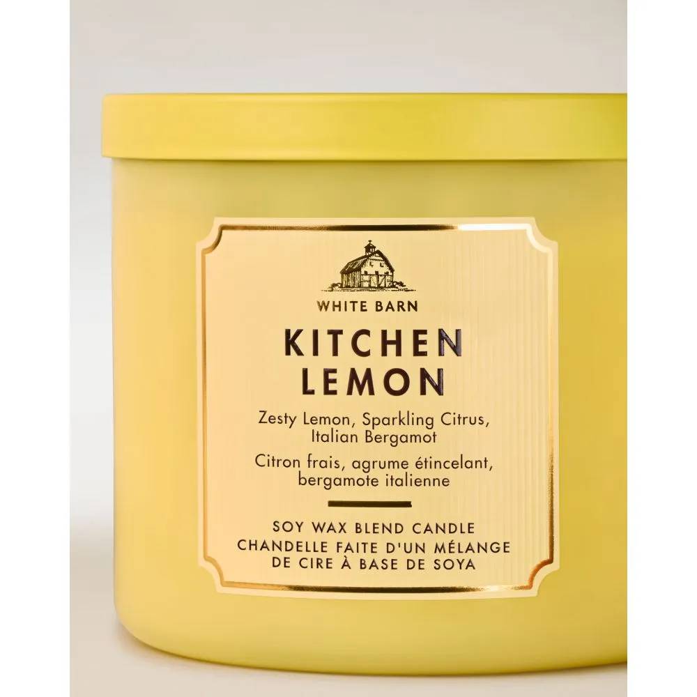 Vela White Barn Kitchen Lemon em pote amarelo claro, com r&oacute;tulo bege e borda dourada. O r&oacute;tulo exibe o nome da marca, uma ilustra&ccedil;&atilde;o de celeiro e a descri&ccedil;&atilde;o do aroma: lim&atilde;o picante, c&iacute;tricos e bergamota italiana, em ingl&ecirc;s e franc&ecirc;s