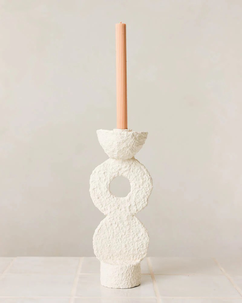 Castical branco texturizado com design abstrato, composto por formas geom&eacute;tricas empilhadas, segurando uma vela rosa p&ecirc;ssego canelada, em fundo claro